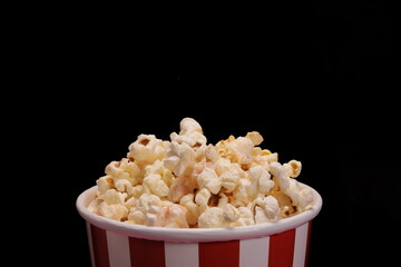 Paper cup with popcorn on black background