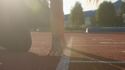 Caucasian woman at the athletic track starting point, hands on the start line and legs on starting block, ready set and go, handheld shot.