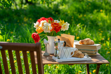 Bouquet of flowers, croissant, cup of tea or coffee, books on table in summer garden. Rest in...