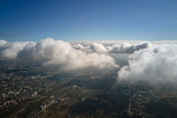 Aerial view from airplane window at high altitude of distant city covered with puffy cumulus clouds...
