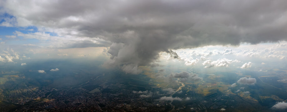 Aerial view from airplane window at high altitude of distant city covered with puffy cumulus clouds forming before rainstorm