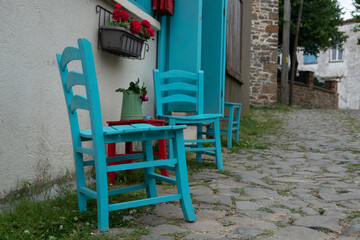 Blue chairs and wooden red stool against a home wall in Gliki, an old Greek village in Gokceada. Canakkale, Turkey. There's a flower pot with red flower on the small stool table