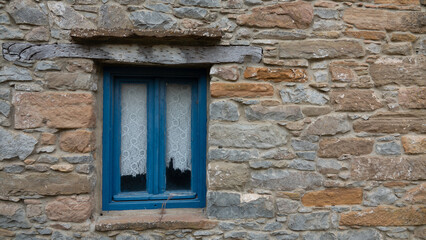 Fototapeta na wymiar Traditional Greece, Mediterranean, Aegean type stone house window with blue blinds