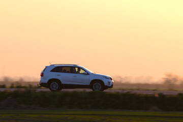 Fototapeta na wymiar SUV car driving fast on intercity road at sunset. Highway traffic in evening