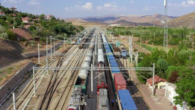 4K drone footage over train station. Aerial shooting of arriving train and parked wagons against village on the hill and mountainous rural landscape background stock video. 