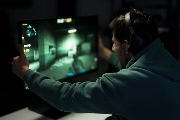 Back view of male cybersport gamer in headset touching computer monitor while celebrating successful game in dark room