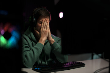 Young disappointed male cybersport gamer sitting at table with prayer hands while playing video game on computer