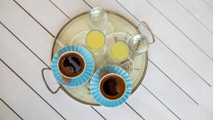 turkish coffee served with a little cookie and lemon liqueur or  limoncello  on tray per two person on white wooden table