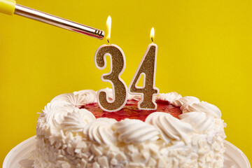 A candle in the form of the number 34, stuck in a holiday cake, is lit. Celebrating a birthday or a...