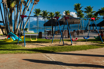 Outdoor playground with toy for children. Coconut trees and the beach in the background. Lush...