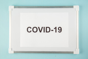 Above view of a sheet with covid- writing on white desk on blue background