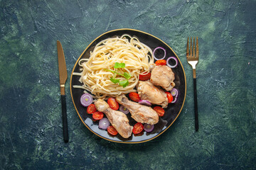 Above view of raw pastas chickens and vegetables on a plate and cutlery set on green black mix colors background