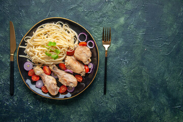 Above view of raw pastas chickens and vegetables on a plate and cutlery set on the right side on green black mix colors background