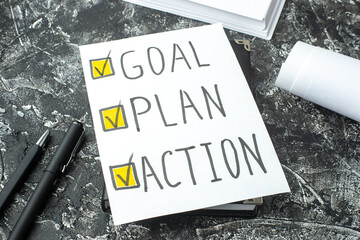Close up view of white sheet with GOAL PLAN ACTION writings ticks on notebook ruler pens blanks on gray distressed background