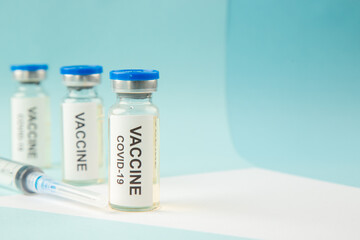 Close up view of COVID- VACCINE in closed ampoules and disposable syringe on the right side on pastel blue and white background with free space