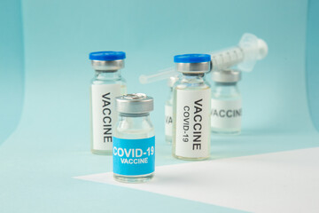 Close up view of COVID- vaccine ampoules and disposable syringe on pastel blue and white background