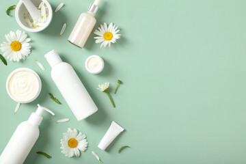 Organic cosmetics skincare products with chamomile flowers on green table. Flat lay, top view.