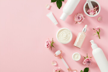 Face skin care products with rose blossoms on pastel pink background. Flat lay, top view.