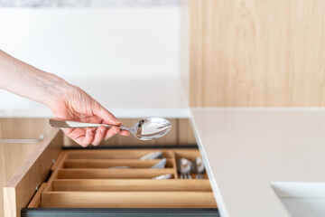 Female hand taking tablespoon over opened cutlery drawer