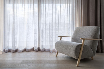 Armchair on hardwood floor against linen curtains on window