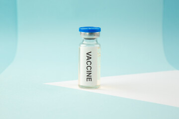 Front close view of COVID- VACCINE in a closed ampoule on blue wave background with free space
