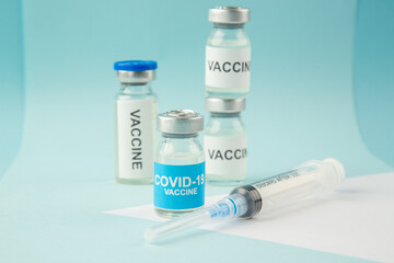 Front close view of COVID- vaccine ampoules and disposable syringe on pastel blue and white background