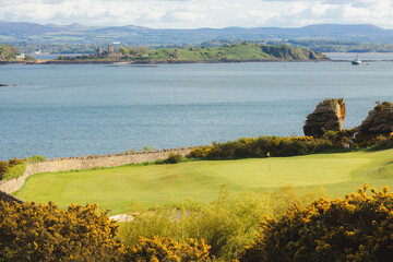 Scenic view of coastal golf hole and green and the Firth of Forth with the historic Inchcolm Abbey...