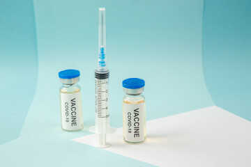 Front close view of vaccine in medical ampoules for Covid- and empty disposable syringe on a white blank on blue background