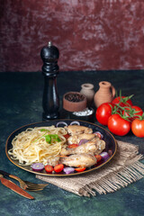 Front close view of raw pastas chickens and vegetables on a plate on nude towel and cutlery set tomatoes spices wooden hammer on green black mix colors background