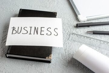 Front view of BUSINESS writing on white sheet on black notebook pens ruler desk blank on gray sand background