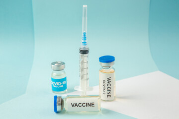 Front view of covid- vaccine in medical ampoules and empty disposable syringe on a white blank on blue background