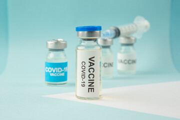 Front view of COVID- vaccine ampoules and disposable syringe on pastel blue and white background
