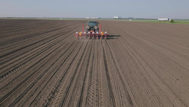 Static shot of a tractor cultivating arable land for seeding crops. Cars driving through the road near agricultural field