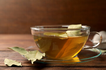 Cup of freshly brewed tea with bay leaves on wooden table, closeup