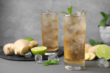 Glass of tasty ginger ale with ice cubes and ingredients on grey wooden table, space for text