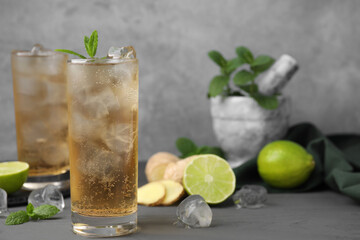 Glass of tasty ginger ale with ice cubes and ingredients on grey wooden table, space for text - obrazy, fototapety, plakaty