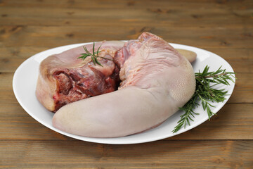 Plate with raw beef tongues and rosemary on wooden table, closeup