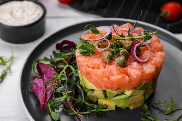 Tasty salmon tartare with avocado and greens on white table, closeup
