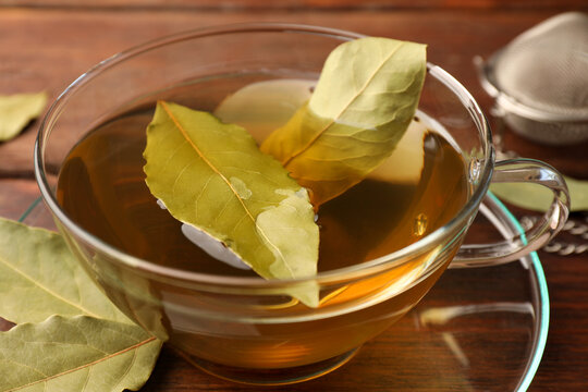 Cup of freshly brewed tea with bay leaves on wooden table, closeup