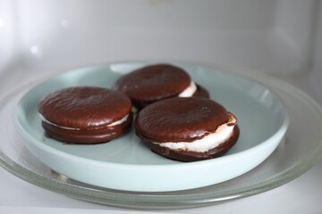 Tasty sweet choco pies on plate in microwave, closeup