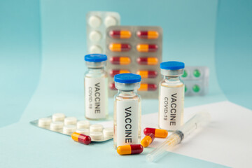 Horizontal view of vaccine in medical ampoules packed pills and capsules for treatment on pastel blue background