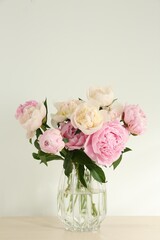 Bouquet of beautiful peonies in glass vase on beige table