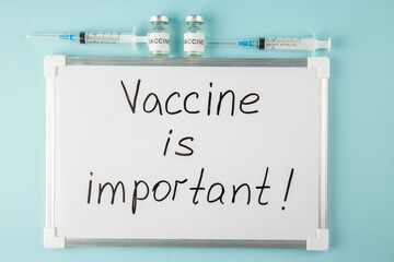 Overhead view of Vaccine is important writing on white desk and medicine in ampoules disposable syringes on blue background