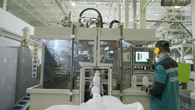 Plant worker setting up the industrial processing machine. Worker pressing buttons on the industrial machine control panel. Worker setting up the industrial machine for the production process.