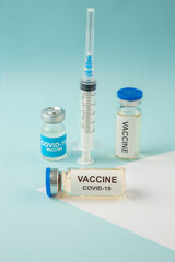 Side view of COVID- vaccine in medical ampoules and disposable syringe on pastel blue and white background