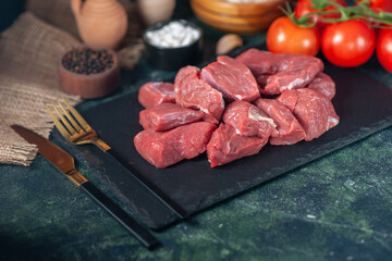 Side view of fresh raw chopped meats and cutlery set tomatoes on wooden board garlics on dark background