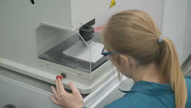 Woman worker operates the small hydraulic press equipment. Worker testing the quality of a hydraulic press machine. Factory worker using a hydraulic press to stamp the white sheet of paper.