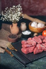 Side view of fresh raw chopped meats and cutlery set tomatoes on wooden board garlics spices on dark background