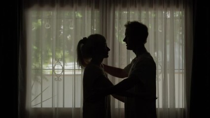 silhouette woman and man share loving hug and say goodbye against room window