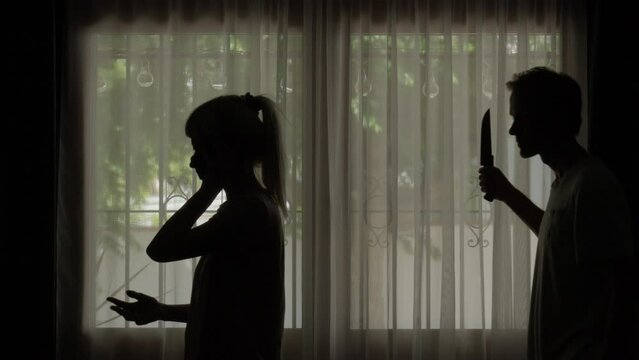 Woman talking on phone, man approaches from behind and stabs he with a knife, against window background